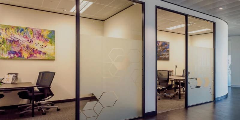 Bright private office interior with glass partitioning, privacy film panels, and modern abstract wall art